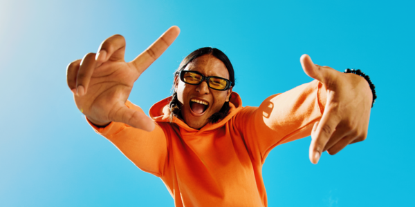 Jongere met zonnebril en feloranje trui die een frame maakt met zijn handen